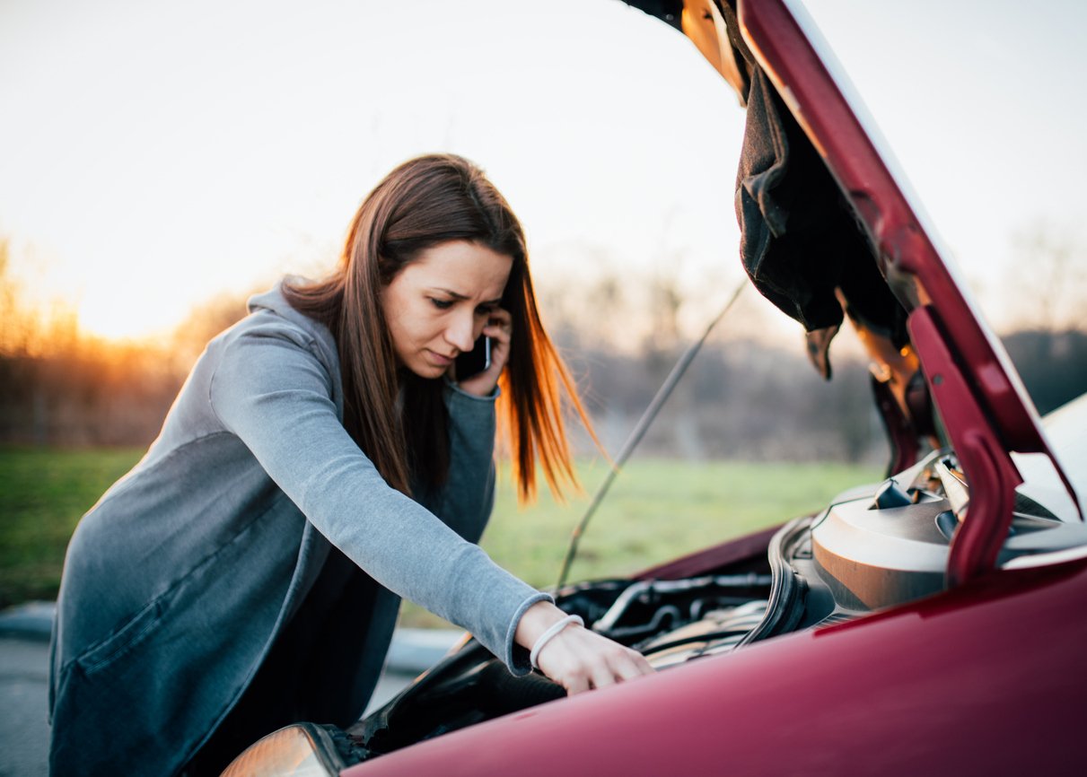 Woman checking under her car’s hood while calling for help, illustrating the value of mechanical breakdown protection coverage.