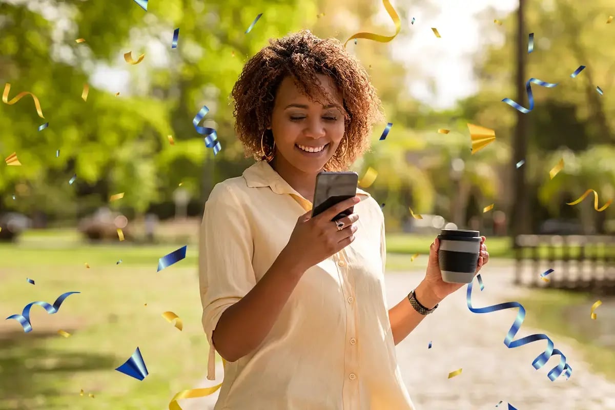 Smiling woman checks her phone outside surrounded by confetti Smiling woman checks her phone outside surrounded by confetti
