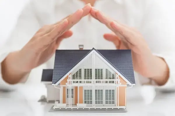 Hands shielding a model home to represent strong homeowners insurance coverage that protects your property and peace of mind.