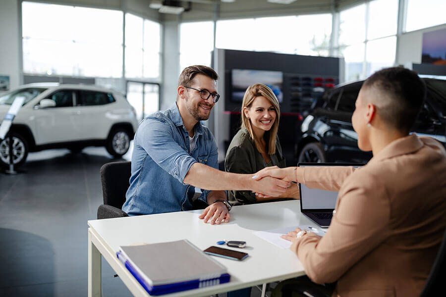 A happy couple signs the paperwork on a car loan even with a 600 credit score.