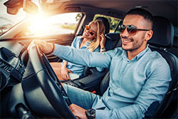 A man and woman in a car driving with sun shining through window