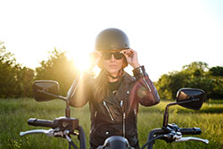 A woman putting on sunglasses sitting on a motorcycle