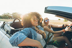 Two women in a convertible with sun behind them